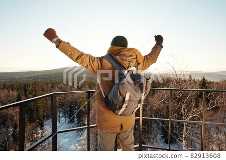 Back view of young backpacker keeping his arms raised Back view of young backpacker keeping his arms raised 82913608