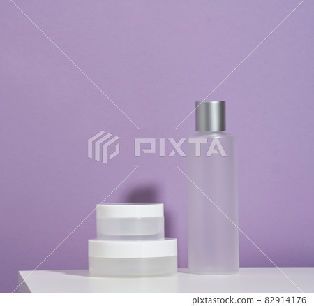 jar and empty white plastic tubes for cosmetics on a purple background. Packaging for cream, gel, serum, advertising and product promotion, mock up jar and empty white plastic tubes for cosmetics on a purple background. Packaging for cream, gel, serum, advertising and product promotion, mock up 82914176