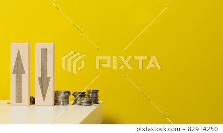 two wooden bars with arrows up and down on the table with coins, yellow background. Falls and increases in prices for utilities two wooden bars with arrows up and down on the table with coins, yellow background. Falls and increases in prices for utilities 82914250