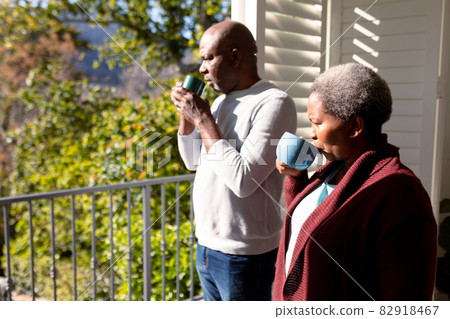 African american senior couple drinking coffee standing on balcony and looking into distance 82918467