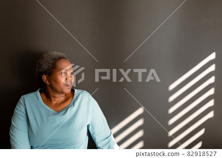 Relaxed african american senior woman sitting at wall in ray of light 82918527