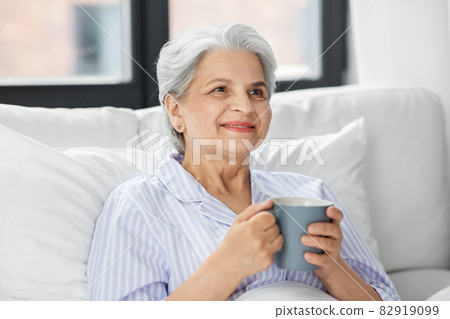 old woman with cup of coffee in bed at home 82919099