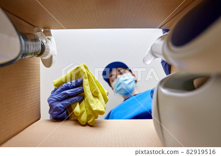 woman in mask packing cleaning supplies in box 82919516