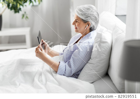 senior woman with tablet pc and earphones in bed 82919551