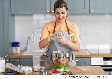 happy young woman cooking food on kitchen at home 82919618