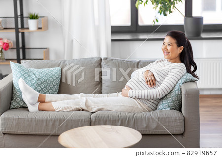 happy pregnant asian woman sitting on sofa at home happy pregnant asian woman sitting on sofa at home 82919657