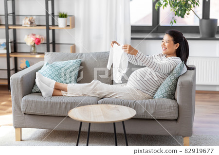 happy pregnant woman with baby's bodysuit at home 82919677