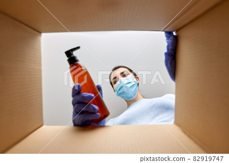 woman in mask unpacking parcel box with cosmetics 82919747