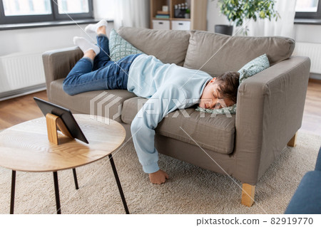 bored man with tablet pc lying on sofa at home bored man with tablet pc lying on sofa at home 82919770