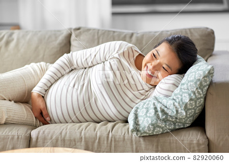 happy pregnant asian woman lying on sofa at home happy pregnant asian woman lying on sofa at home 82920060