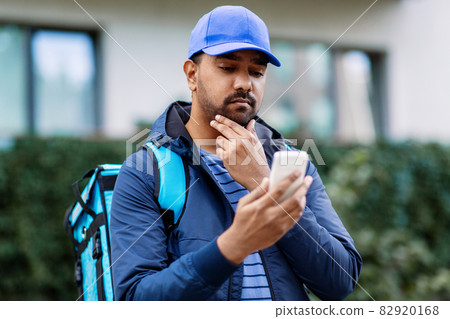 indian delivery man with bag and phone 82920168