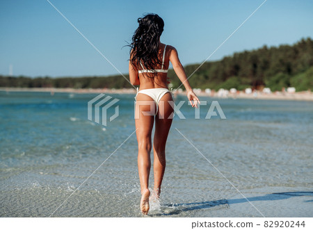 young woman in bikini swimsuit running on beach - Stock Photo