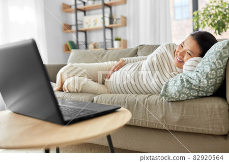 happy pregnant asian woman with laptop at home 82920564