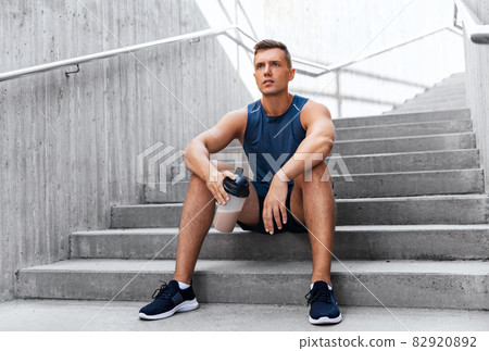 sportsman with shake in bottle sitting on stairs sportsman with shake in bottle sitting on stairs 82920892