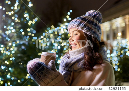 happy woman drinking coffee over christmas lights 82921163