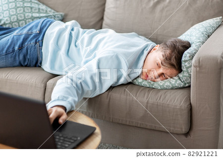 bored man with laptop lying on sofa at home 82921221