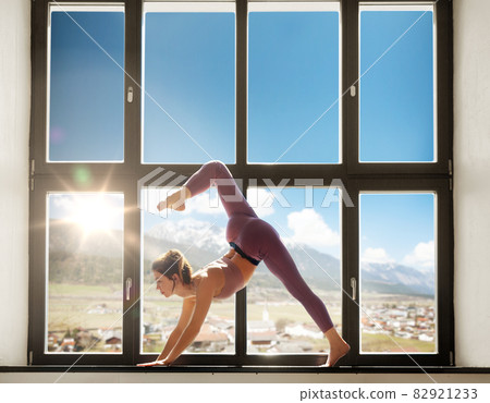 woman doing yoga exercise on window sill at studio 82921233