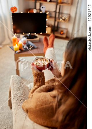 woman watches tv and drinks cocoa on halloween woman watches tv and drinks cocoa on halloween 82921745