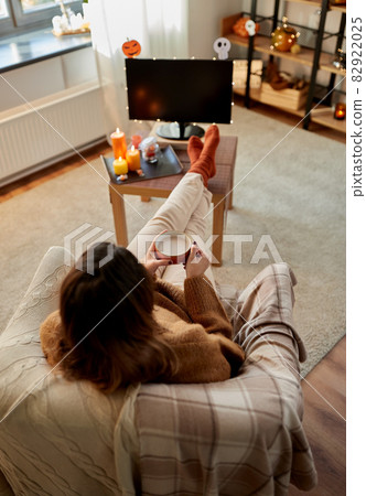 woman watches tv and drinks cocoa on halloween woman watches tv and drinks cocoa on halloween 82922025
