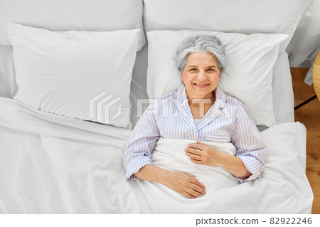 smiling senior woman lying in bed at home bedroom 82922246