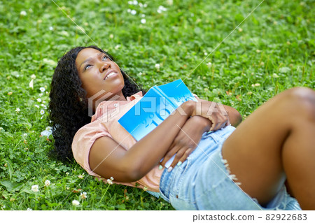 african student girl with textbook lying on grass 82922683