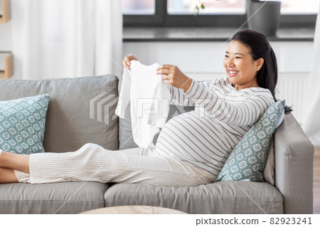 happy pregnant woman with baby's bodysuit at home 82923241