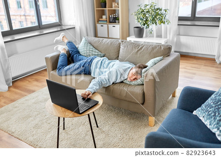 bored man with laptop lying on sofa at home 82923643