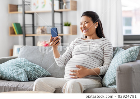 pregnant woman with phone and earphones at home pregnant woman with phone and earphones at home 82924781