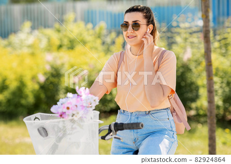 happy woman with earphones riding bicycle in city 82924864