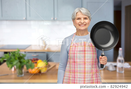 smiling senior woman in apron with frying pan 82924942