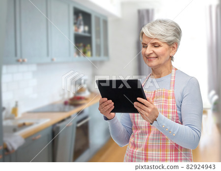 smiling senior woman in apron with tablet computer smiling senior woman in apron with tablet computer 82924943