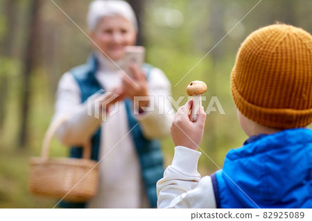 grandmother photographing grandson with mushroom 82925089