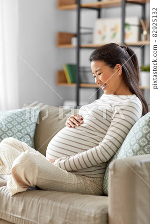 happy pregnant asian woman sitting on sofa at home happy pregnant asian woman sitting on sofa at home 82925132