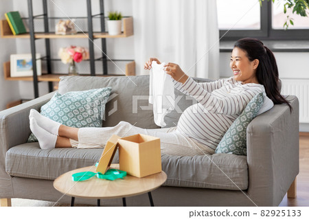 happy pregnant woman with baby's bodysuit at home happy pregnant woman with baby's bodysuit at home 82925133