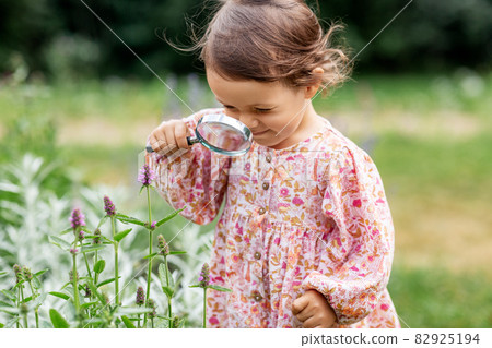baby girl with magnifier looking at garden flowers baby girl with magnifier looking at garden flowers 82925194