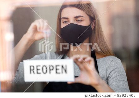 woman in mask with reopen banner on door glass woman in mask with reopen banner on door glass 82925405