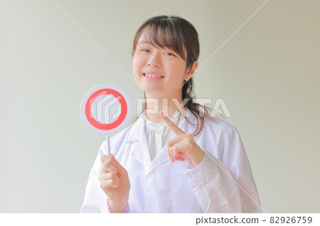 一個穿著白大褂的女人拿著一盤〇,微笑著指著 1 一個穿著白大褂的女人拿著一盤〇,微笑著指著 1 82926759
