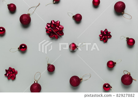 Pattern on gray background with small red Christmas balls or sphere toys, ribbon bows for fir tree. Concept for festive greeting card or invitation for Christmas eve celebration. High quality photo Pattern on gray background with small red Christmas balls or sphere toys, ribbon bows for fir tree. Concept for festive greeting card or invitation for Christmas eve celebration. High quality photo 82927882
