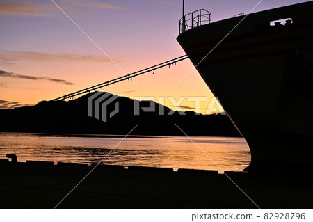 The dawn of Saigo Port on the Oki Islands, the silhouette of the ferry and the mountains behind it, the orange sky and the calm sea The dawn of Saigo Port on the Oki Islands, the silhouette of the ferry and the mountains behind it, the orange sky and the calm sea 82928796