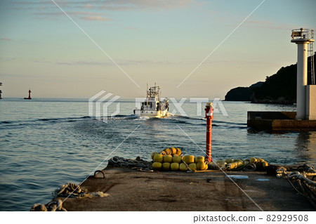 Okinoumi-cho, Oki-gun, Shimane Prefecture Okinoumi Sea Squid fishing boat leaving the Okishima-cho fishing port Pier and white lighthouse illuminated by the setting sun Blue sky 82929508