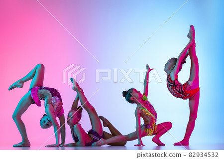 Group of beautiful flexible rhythmic gymnastics artists, girls in sport event isolated on gradient pink blue studio background in neon light 82934532