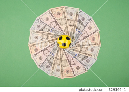 Football little ball lying on mandala kaleidoscope from money. Money and soccer ball - sport and business background. Football little ball lying on mandala kaleidoscope from money. Money and soccer ball - sport and business background. 82936641