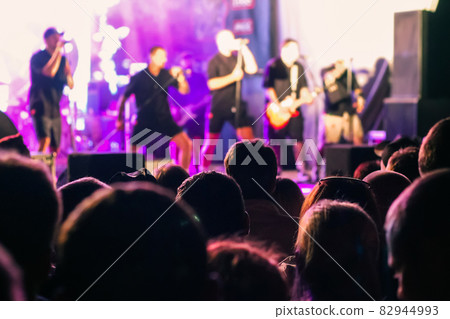 A crowd of people watching a musical group performing on stage 82944993