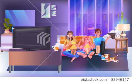 Family sitting on couch watching tv and eating popcorn happy parents and daughter spending time together 82946147