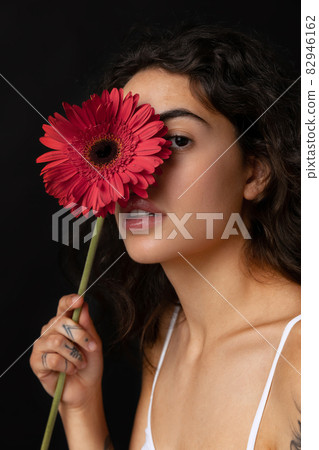 Cropped close-up portrait of beautiful tender woman with red gerberas posing isolated over dark background. Naturality Cropped close-up portrait of beautiful tender woman with red gerberas posing isolated over dark background. Naturality 82946162