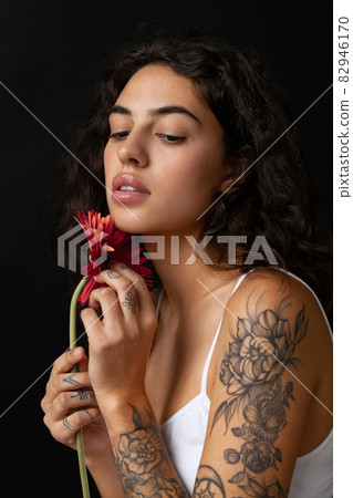 Cropped close-up portrait of beautiful tender woman with red gerberas posing isolated over dark background 82946170
