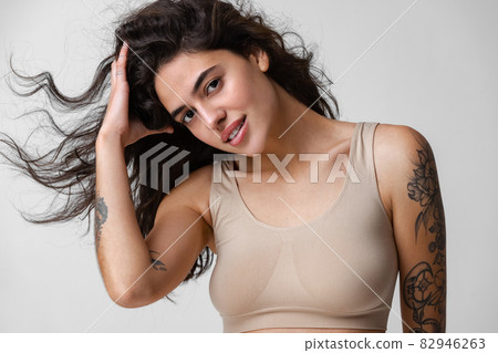 Cropped horizontal portrait of young woman with curly hair and nude makeup in beige inner wear isolated over gray background Cropped horizontal portrait of young woman with curly hair and nude makeup in beige inner wear isolated over gray background 82946263