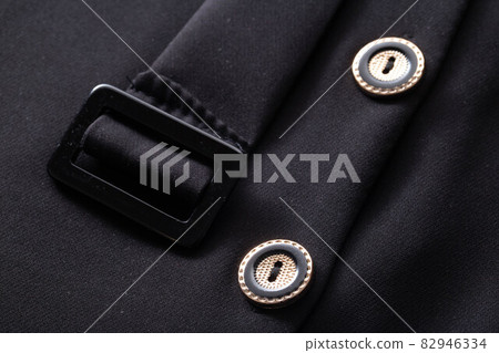 Black stylish clothes with buttons and a belt, background. Dress for woman, macro, material 82946334
