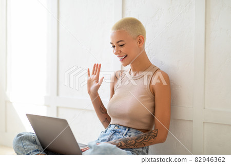 Online chat. Smiling caucasian lady making video call via laptop, waving hand to webcam, sitting over white wall Online chat. Smiling caucasian lady making video call via laptop, waving hand to webcam, sitting over white wall 82946362