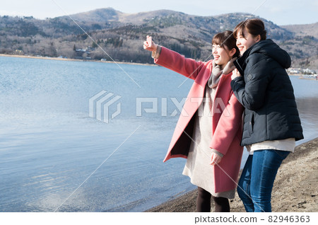 Two women taking selfies on the shores of Lake Yamanaka in winter 82946363